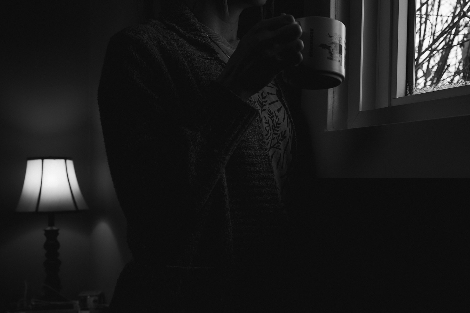 Woman sitting quietly beside a window, reflecting in a softly lit room