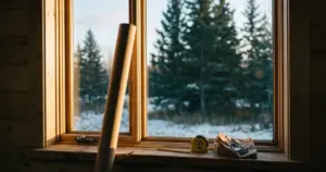 Unopened curtain rod leaning against a bare window with a tape measure on the sill, illustrating the ADHD planning trap between imagining and starting
